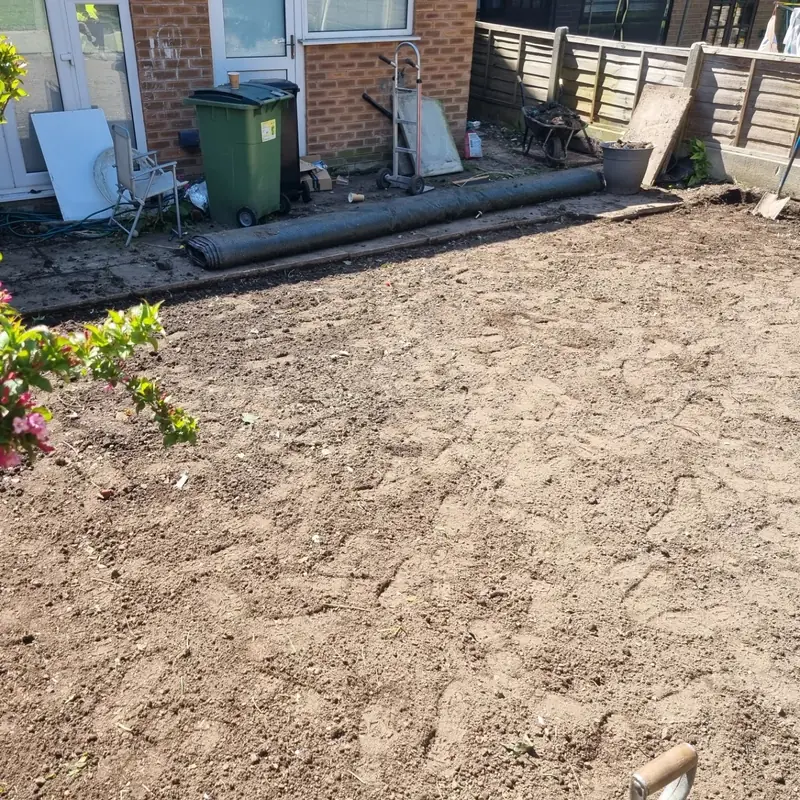 The same garden cleared to bare levelled ground, with a roll of artificial grass waiting by the house