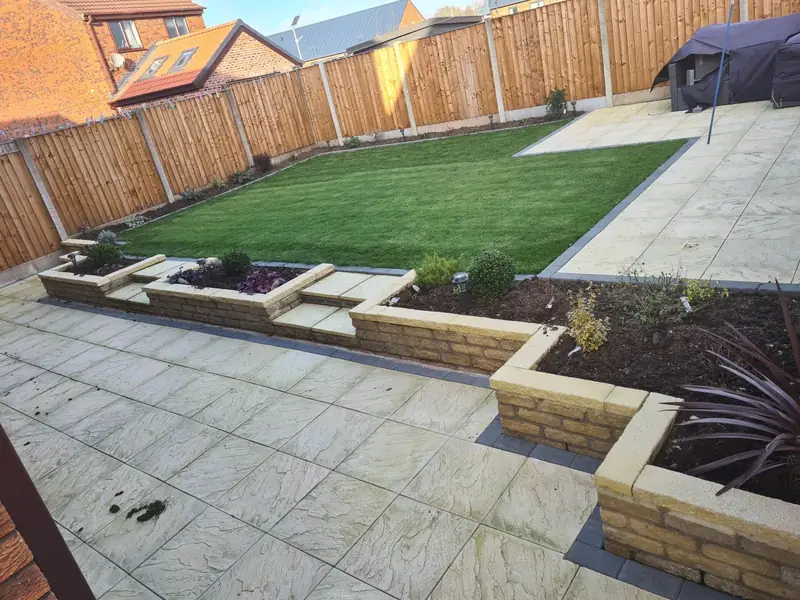 Back garden makeover with a buff riven patio, stepped raised beds in buff walling, a new lawn and closeboard fencing