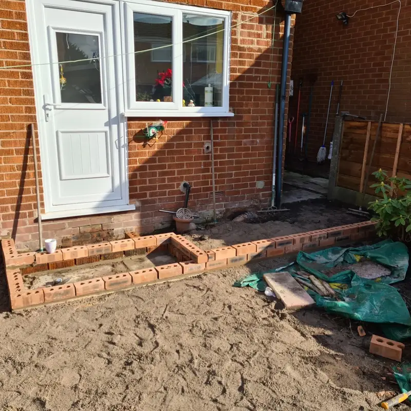 Brick edging being built along the back of a house to form the edge of a new patio and step