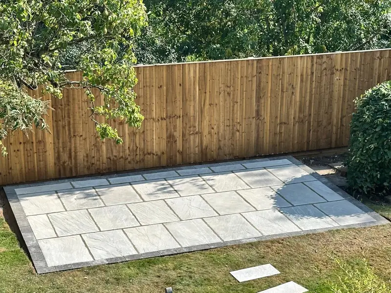 Grey paving slabs with a charcoal block border laid in a lawn, in front of a new feather edge fence